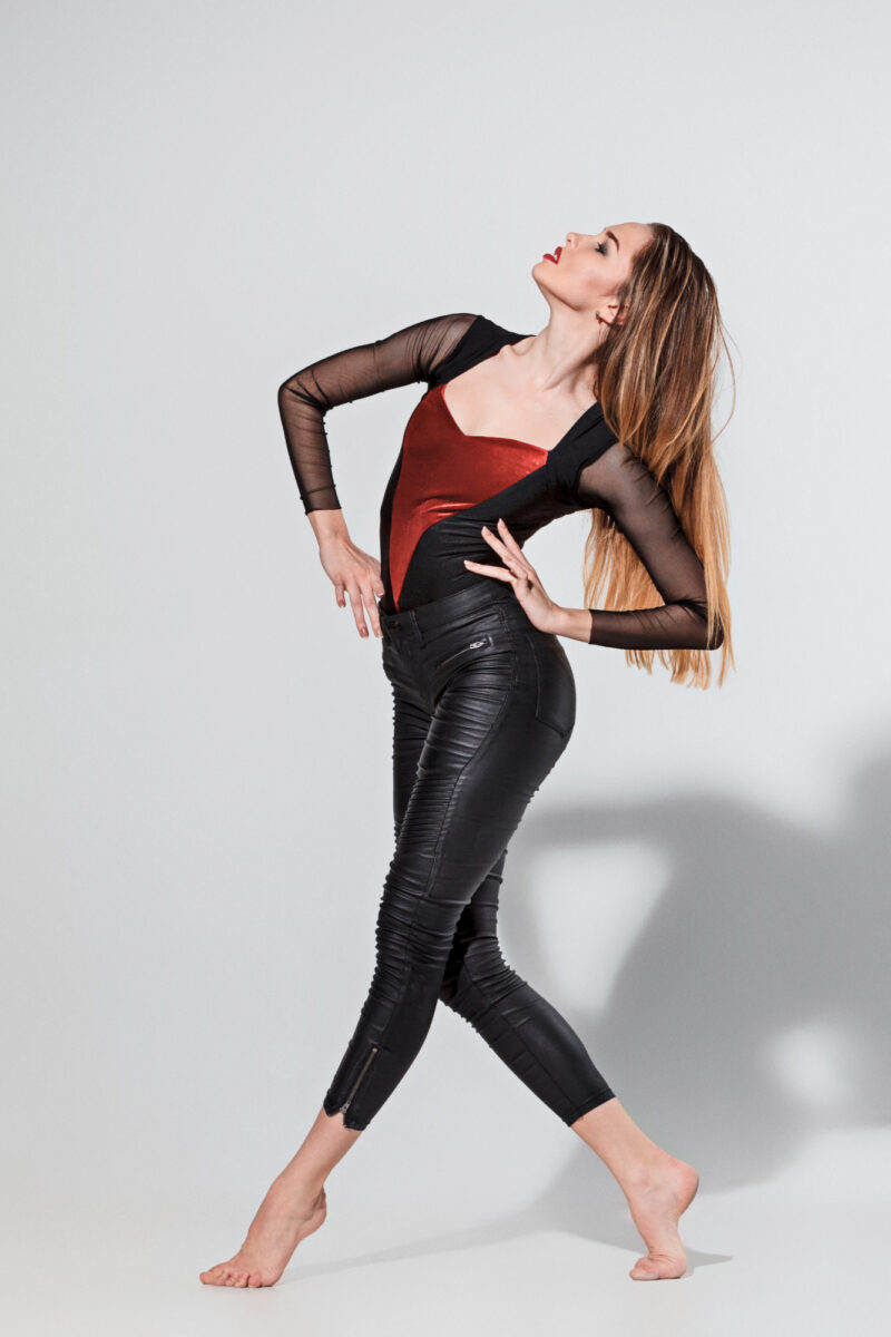 A woman wearing red and black long sleeves and black leather leggings making a pose