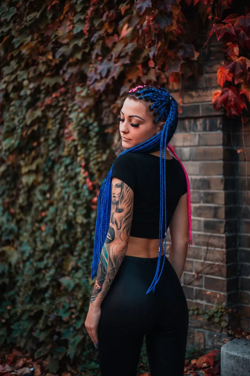 A woman with braided blue and pink hair wearing black crop top and wet look leggings